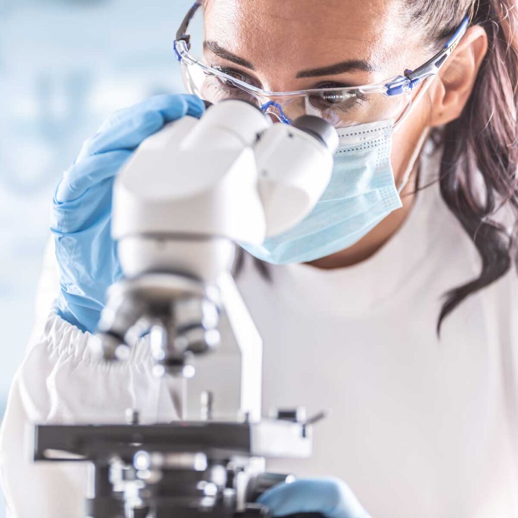 Lab scientist in safety glasses using a microscope