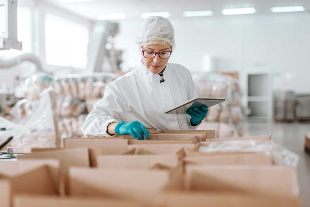 Technician in protective gear checking a tablet on a supplement packing line